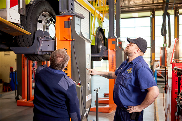 Two workshop staff examining a raised fire truck